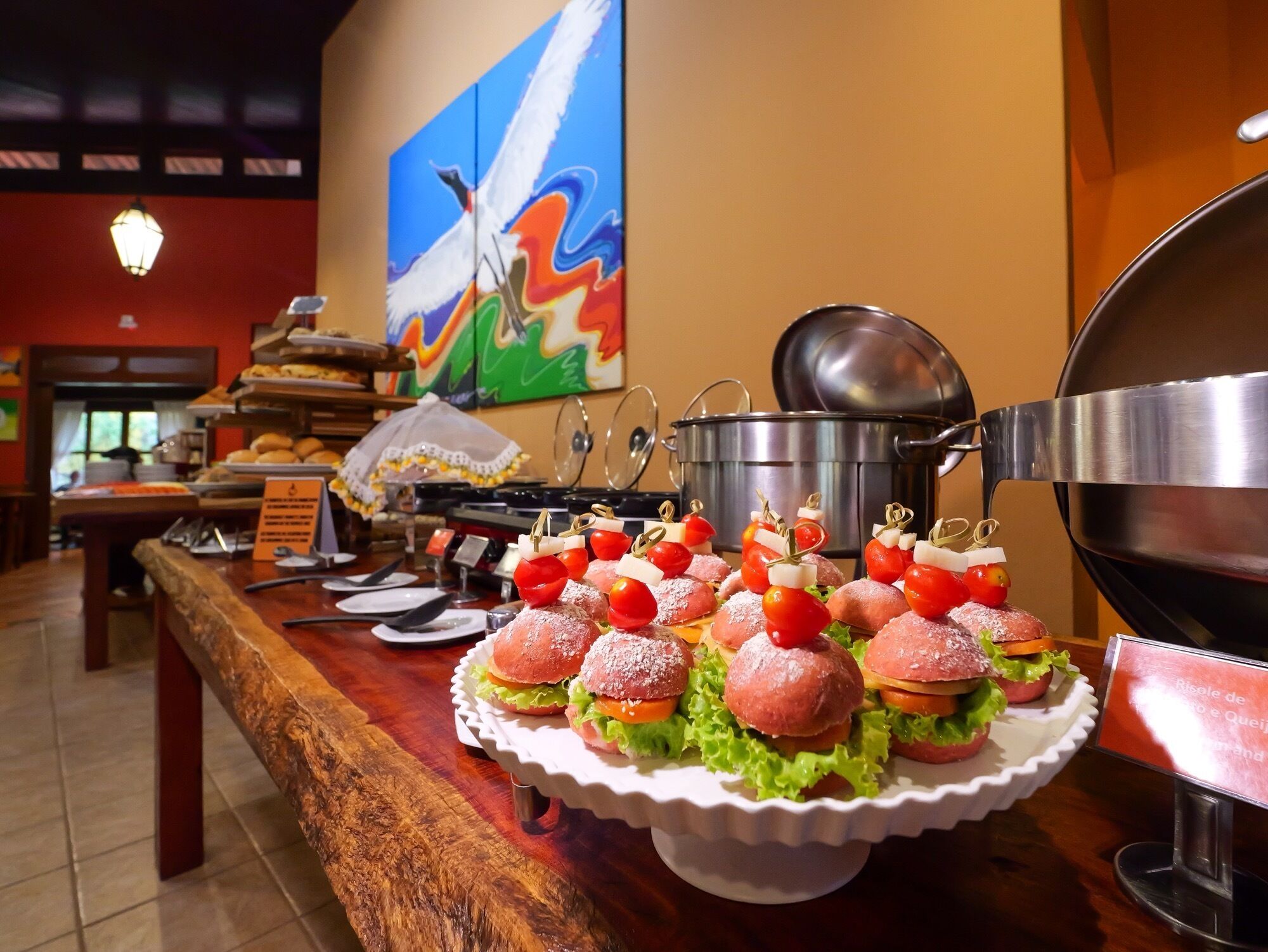 A buffet table with sandwiches, a grill, and a painting on the wall.