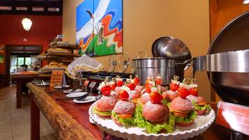 A buffet table with sandwiches, a grill, and a painting on the wall.