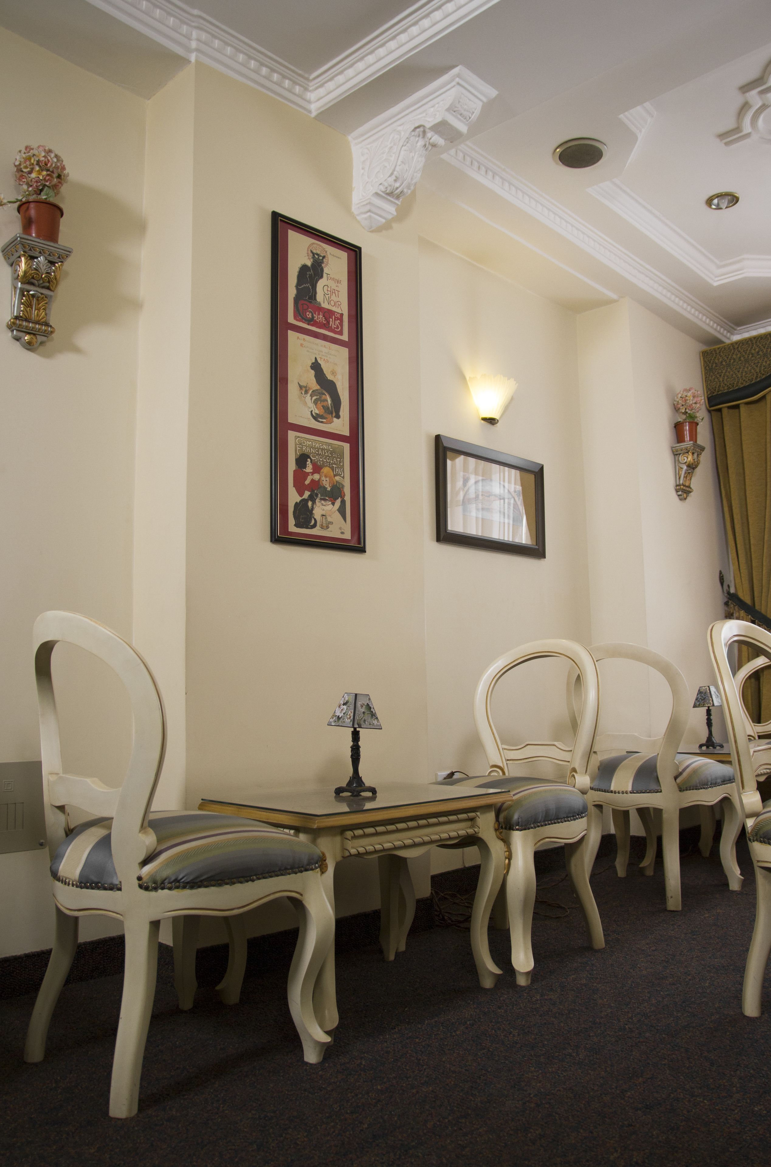 A room with a dining table, four chairs, a lamp, and framed pictures on the wall.