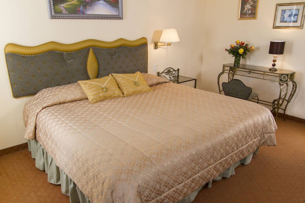 A neatly made bed with a patterned bedspread and two pillows, a bedside table with a lamp, and a small chair.