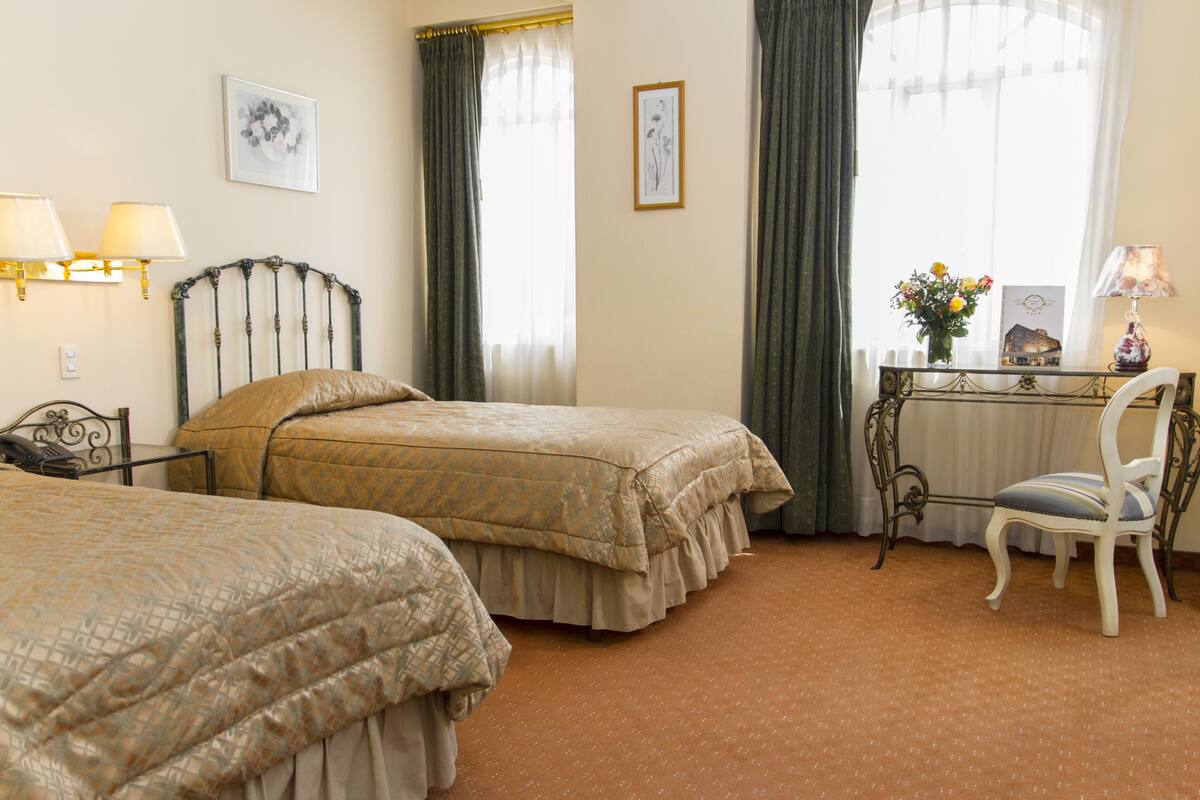A hotel room with two beds, a desk with a chair, and a window with curtains.