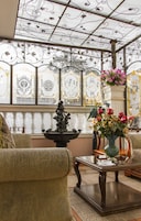 Um solário com painéis de vidro ornamentados, uma fonte e um vaso de flores.