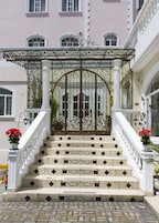 Escadaria ornamentada com azulejos brancos que leva a um portão com detalhes em ferro.