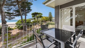 A balcony with a glass table and chairs overlooking a beach and forested area. - Mantra Lorne (Lorne)