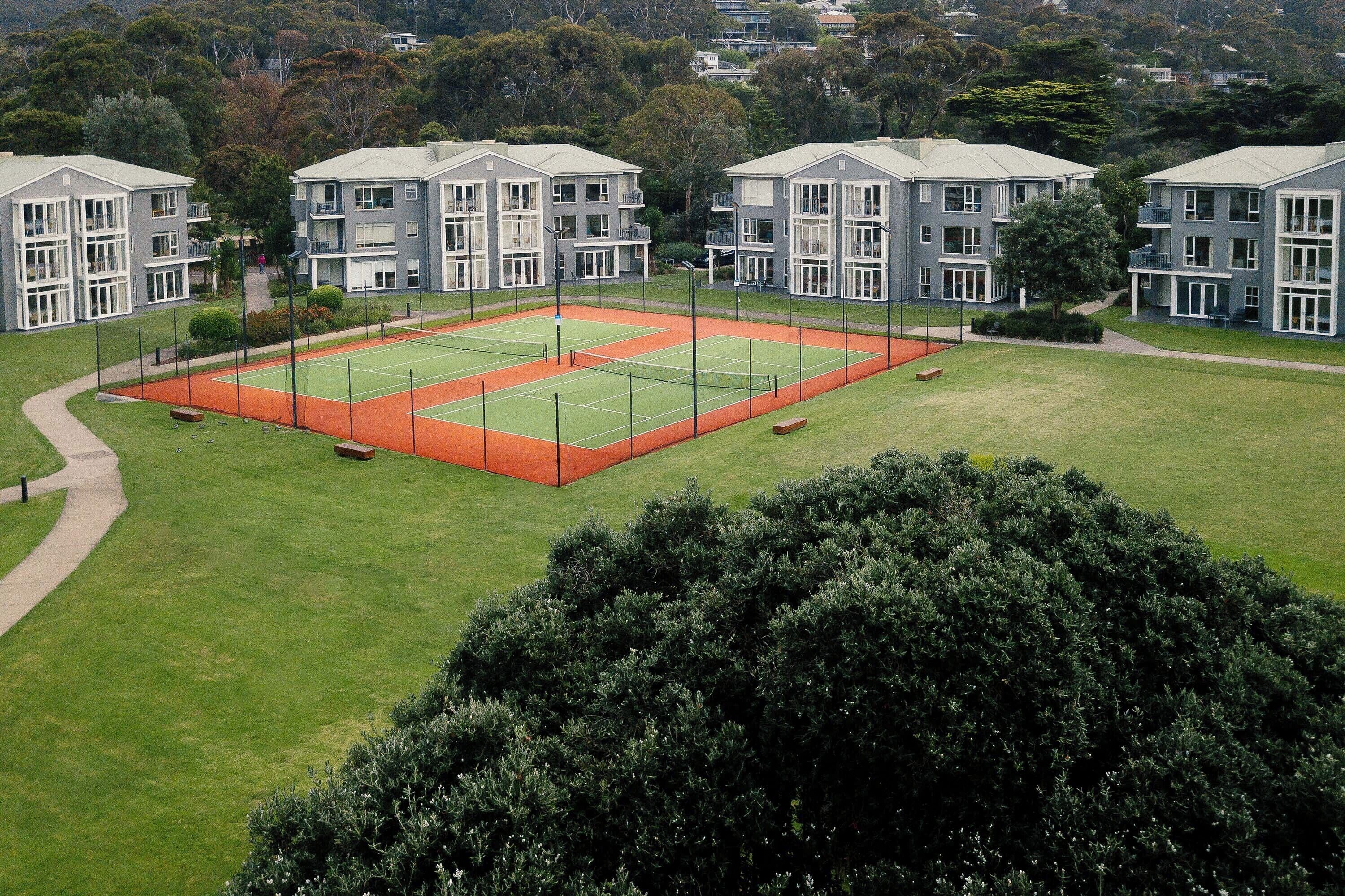 Una cancha de tenis rodeada de edificios modernos con varios pisos y balcones.