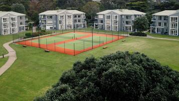 Una cancha de tenis rodeada de edificios modernos con varios pisos y balcones.