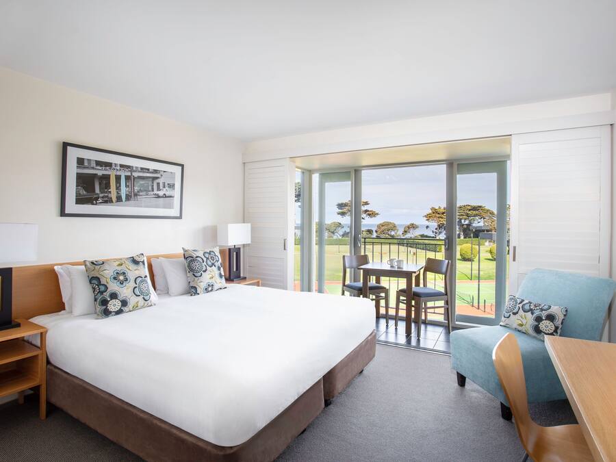 A hotel room with a large bed, a desk, a chair, and a balcony with a view of the outdoors.