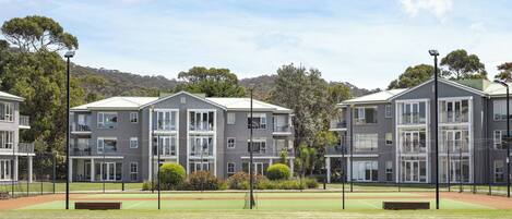A residential building complex with multiple apartment buildings, a tennis court, and surrounding greenery.