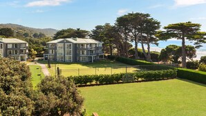 A residential building with a tennis court, surrounded by lush greenery and a view of the sea. - Mantra Lorne (Lorne)