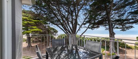 A balcony with a table and chairs, overlooking a beach and ocean.