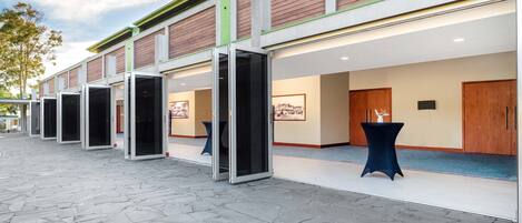 L'ingresso di un hotel con diverse porte aperte, un vialetto lastricato in pietra e un'area reception con tavolo e sedie.