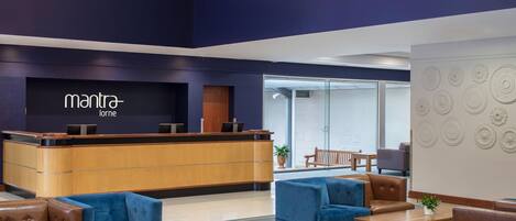 A reception area with a wooden desk, blue sofas, and a potted plant.