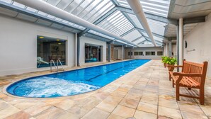 An indoor swimming pool with a glass ceiling, tiled floor, and wooden benches along the side. - Mantra Lorne (Lorne)