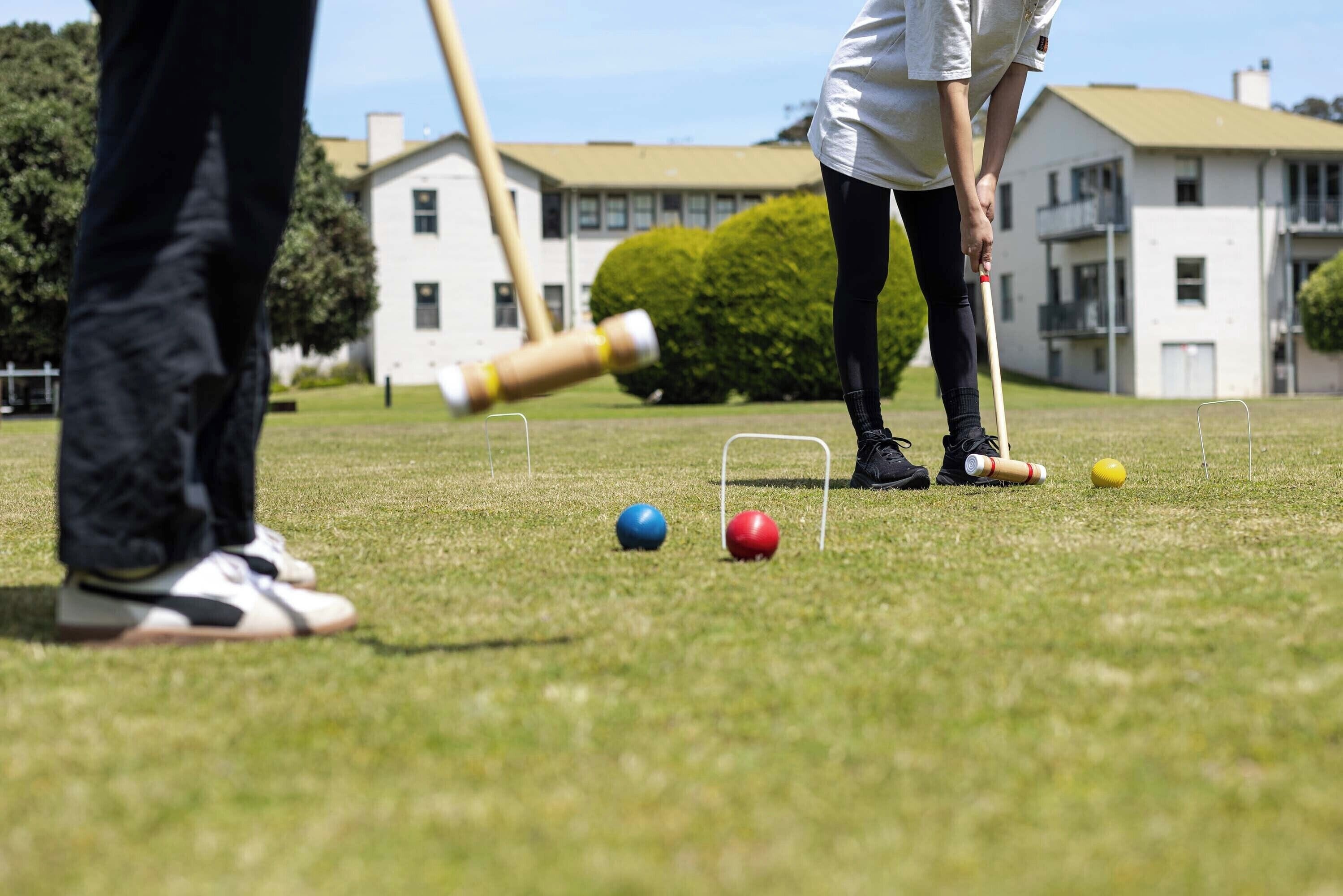 A croquet game in progress on a grassy field with a house in the background.