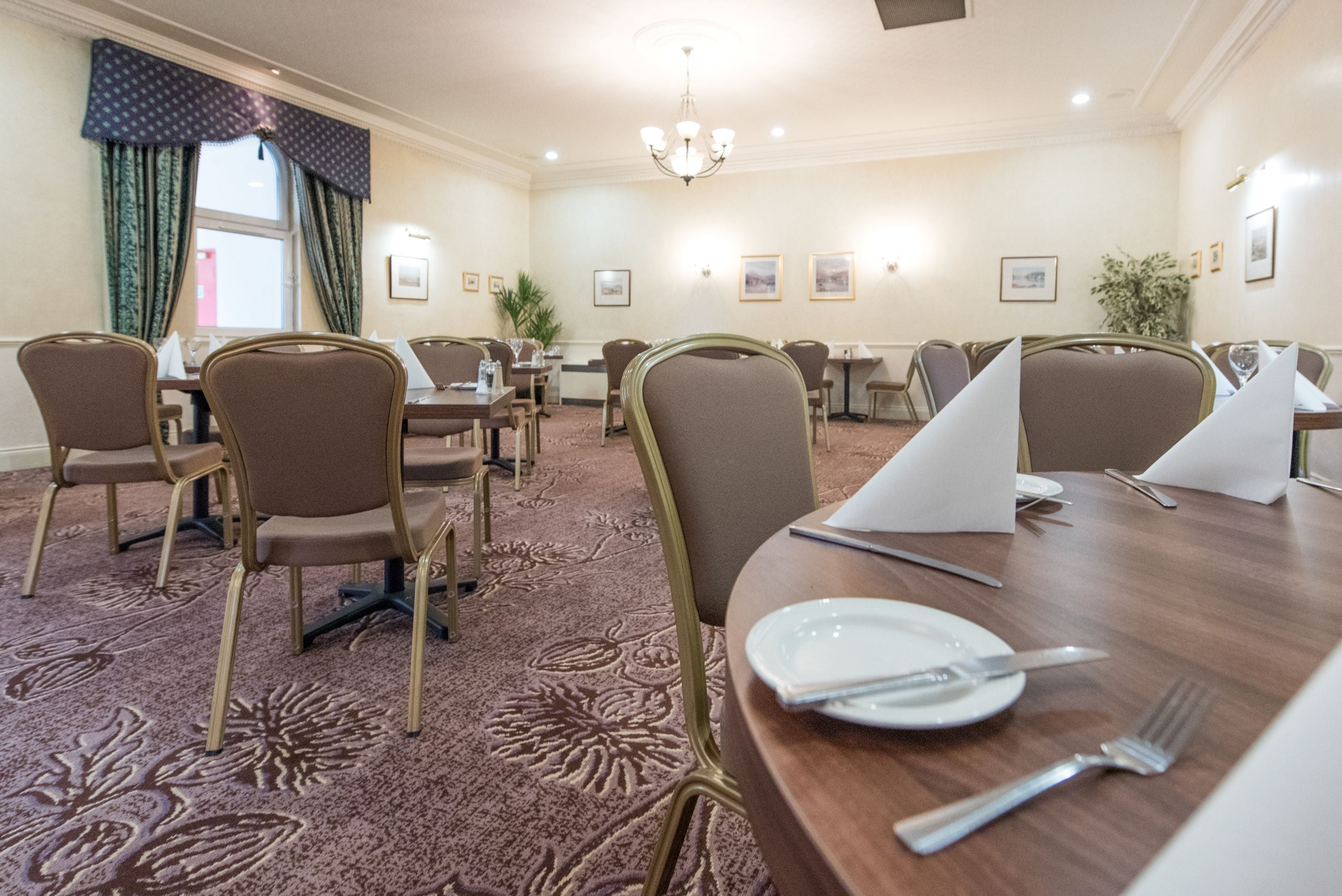 A conference room with round tables and chairs, floral carpet, and framed pictures on the walls.