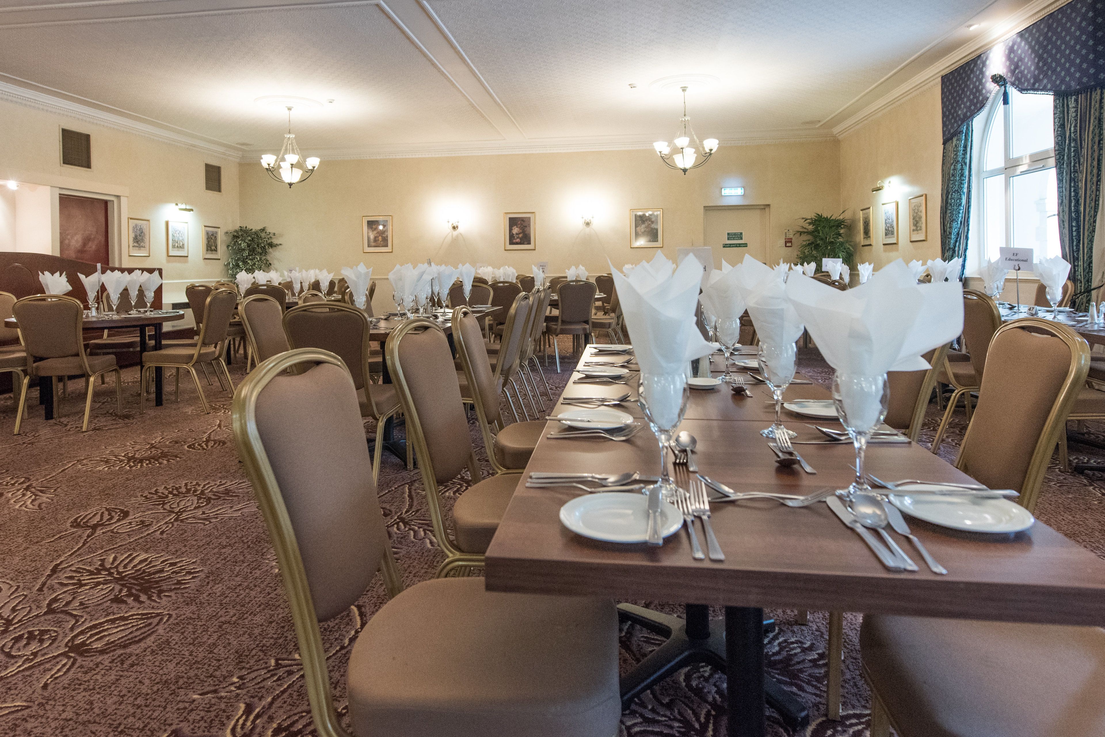Un salón de banquetes con múltiples mesas dispuestas para comer, cada una con servilletas blancas, cubiertos y cristalería.
