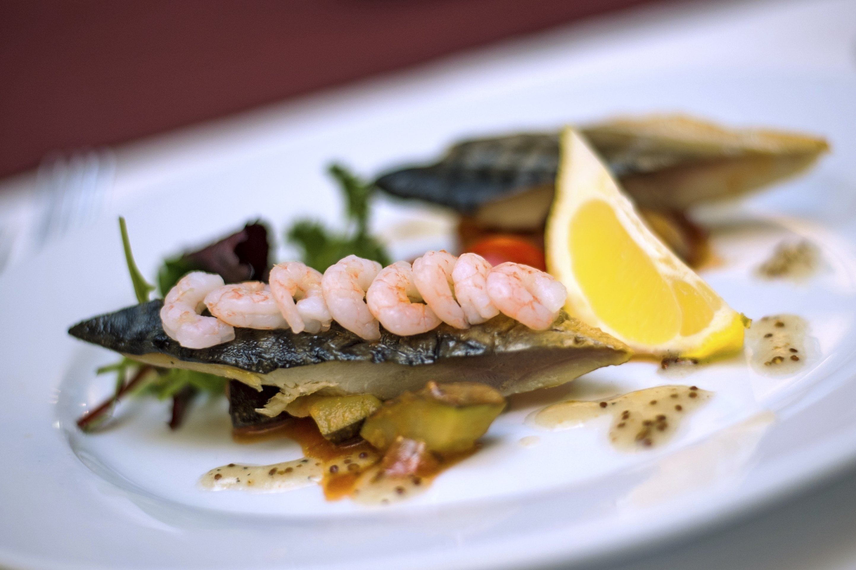 A seafood dish with shrimp on a fish, lemon, and vegetables on a white plate.