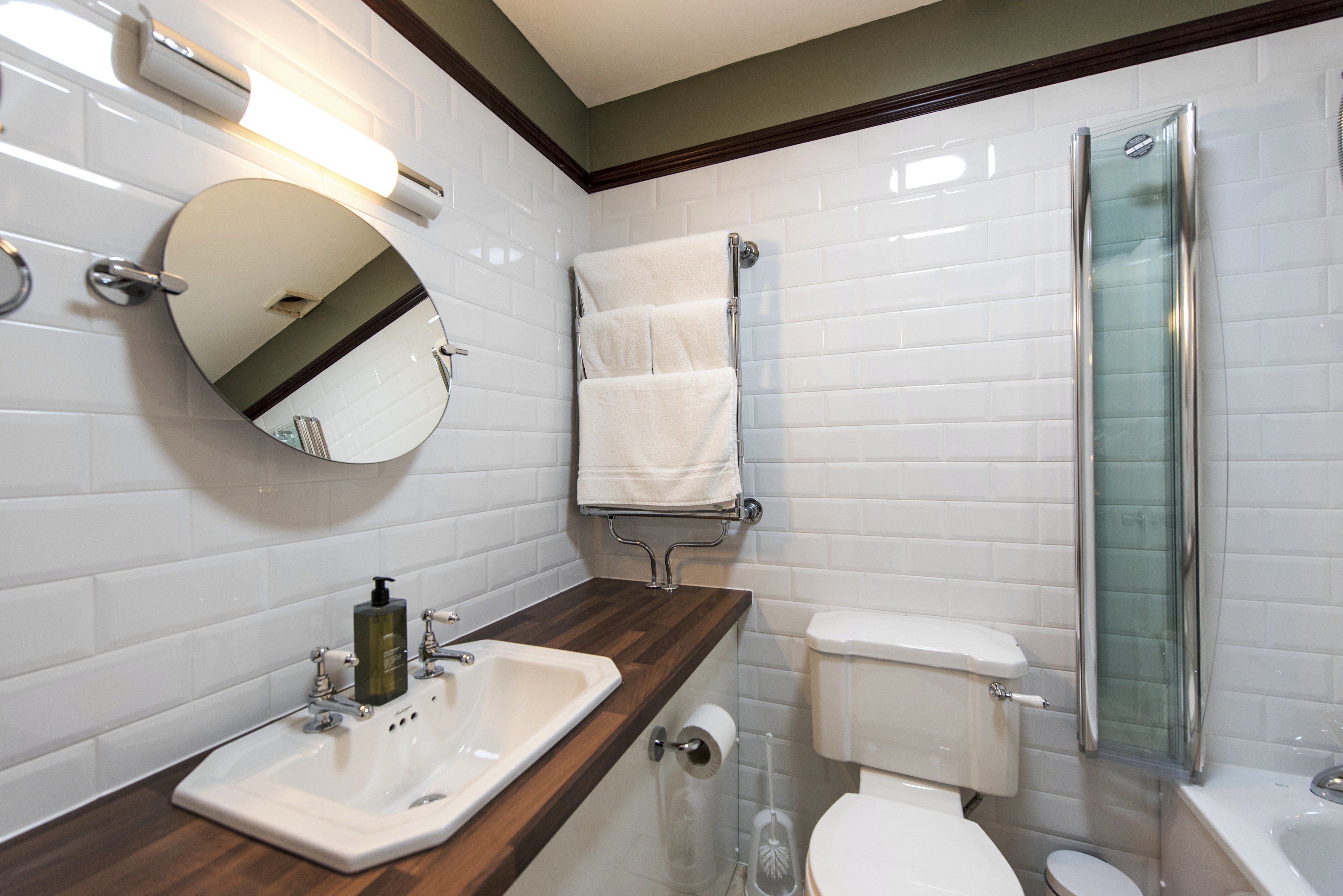 A modern bathroom with a wooden vanity, a round mirror, a toilet, and a glass shower enclosure.