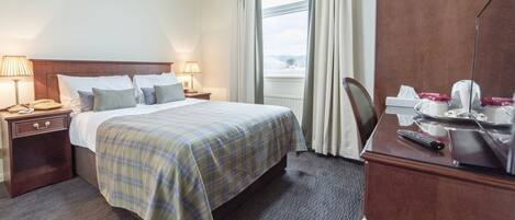 Une chambre d’hôtel comprenant un lit, deux tables de chevet avec des lampes, un bureau avec une chaise et une fenêtre avec des rideaux.