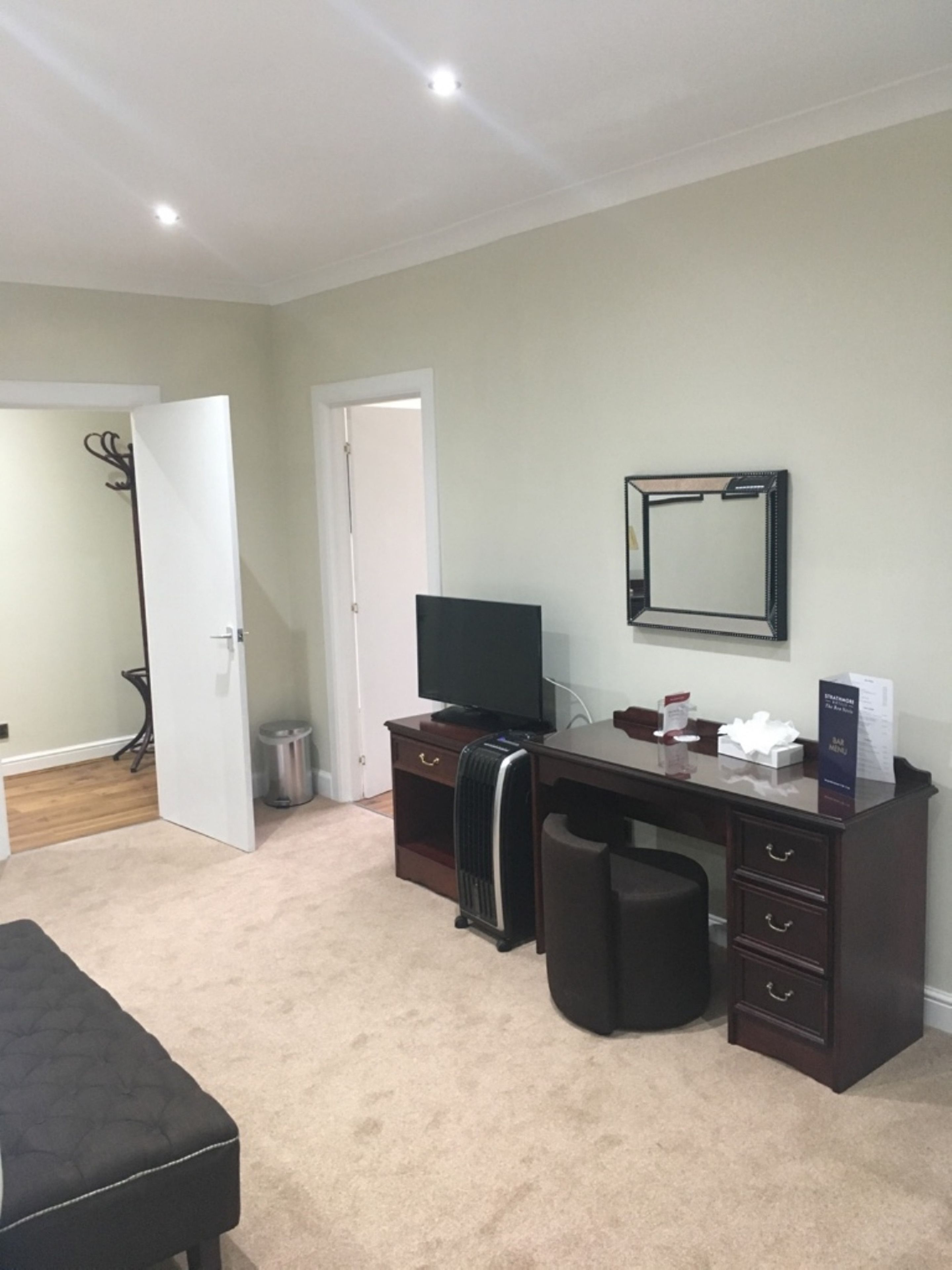 A bedroom with a bed, a desk, a chair, a TV, and a mirror.