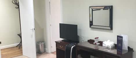 A bedroom with a bed, a desk, a chair, a TV, and a mirror.