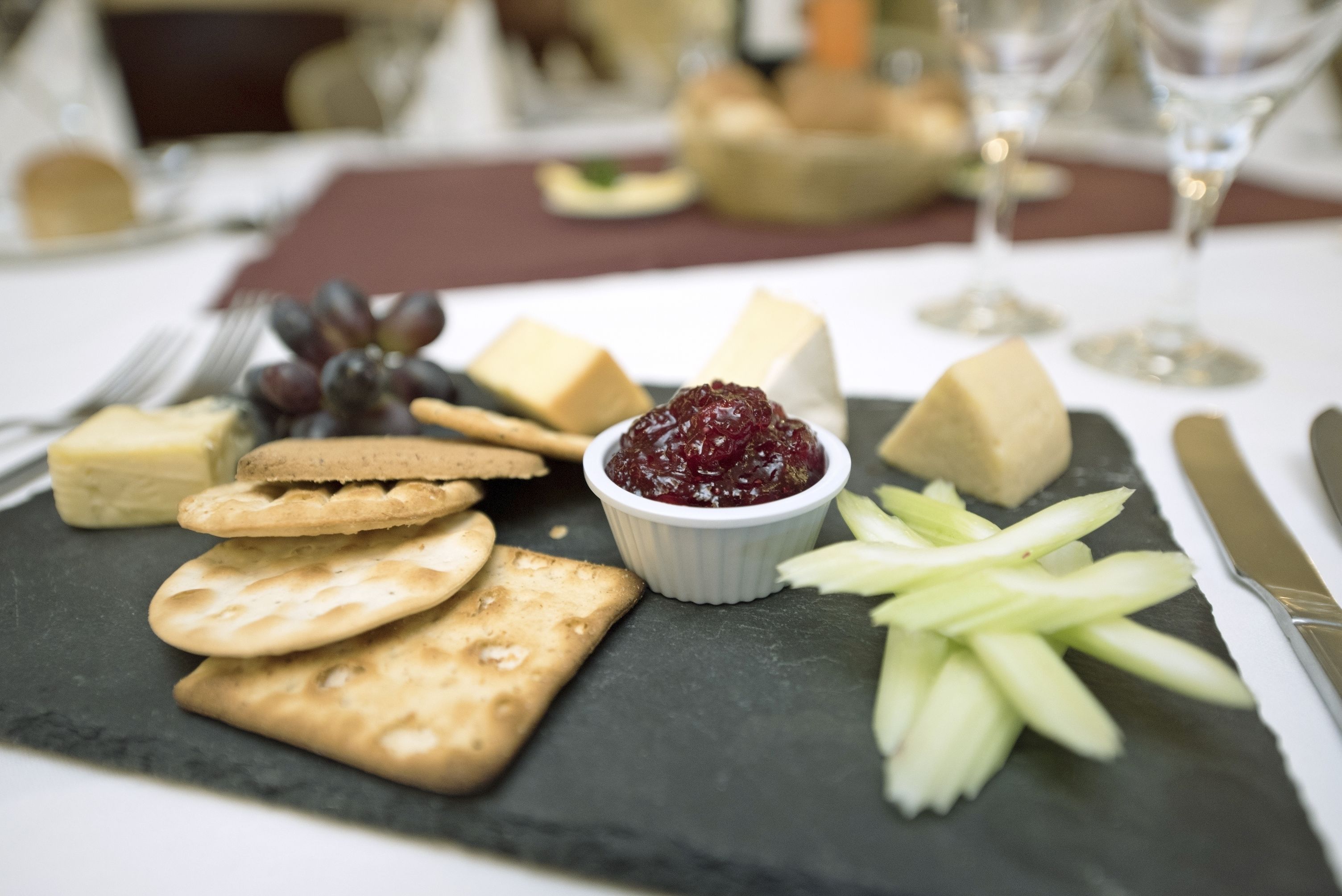 Een kaasplank met crackers, druiven en een klein schaaltje cranberrysaus op een leisteenplank.