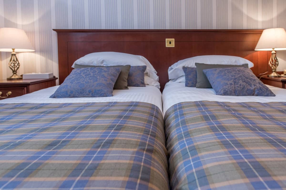 A double bed with plaid bedding, two bedside tables with lamps, and a wooden headboard.