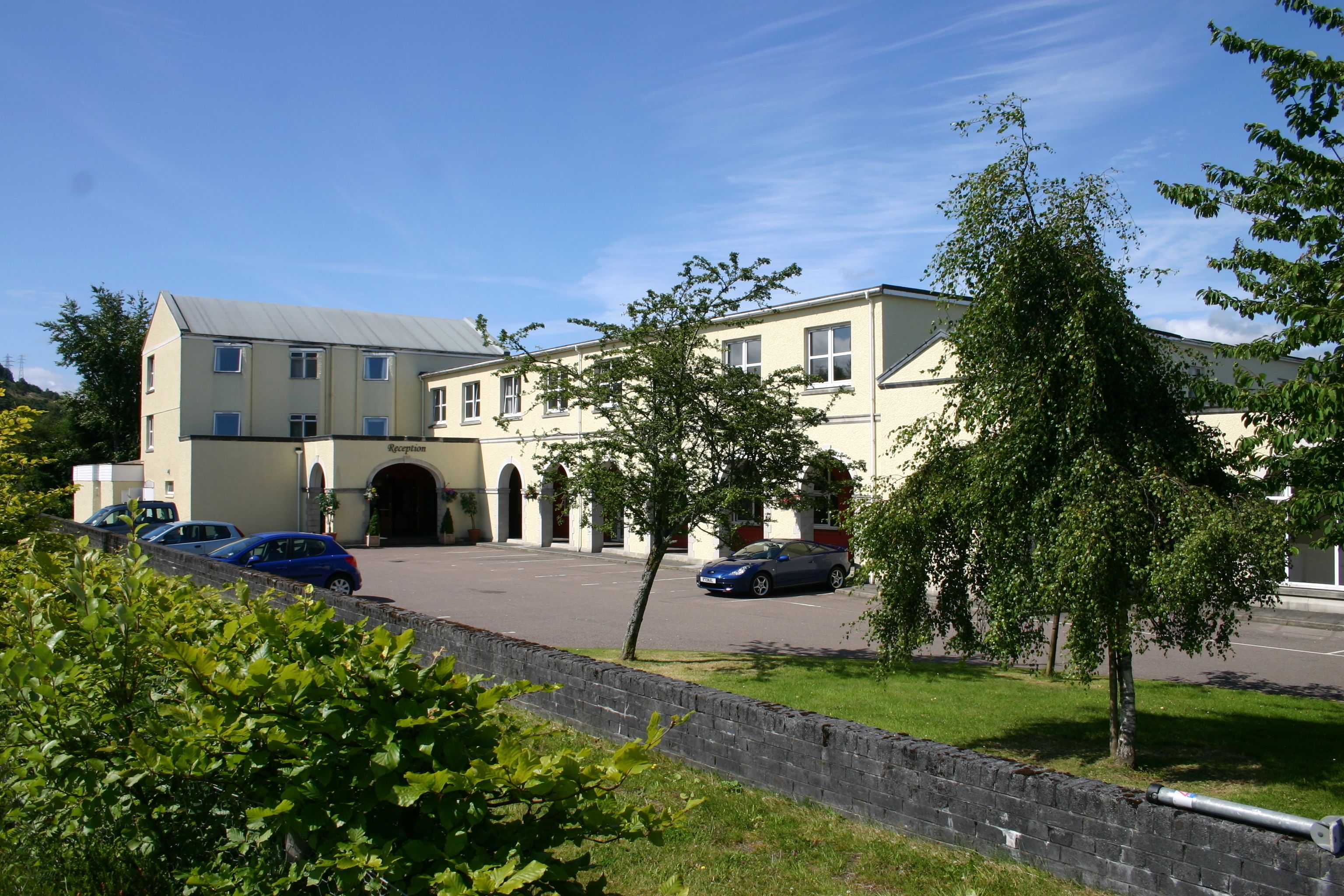 A building with a large entrance, parked cars, and a stone wall in the foreground.
