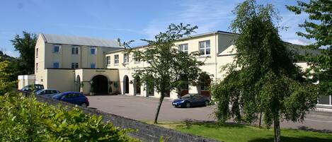 A building with a large entrance, parked cars, and a stone wall in the foreground.
