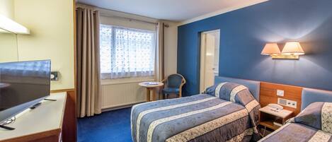 Een hotelkamer met een groot bed, een bureau met een televisie, een kleine tafel en een raam met gordijnen.