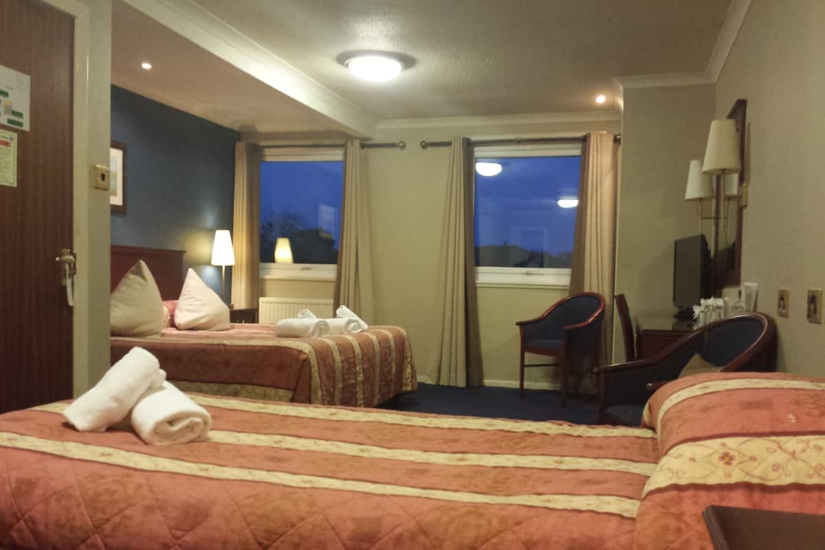 A hotel room with two beds, a desk, a chair, and a window with curtains.