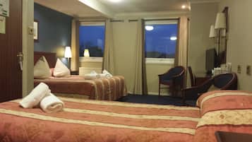 Une chambre d’hôtel avec deux lits, un bureau, une chaise et une fenêtre avec des rideaux.