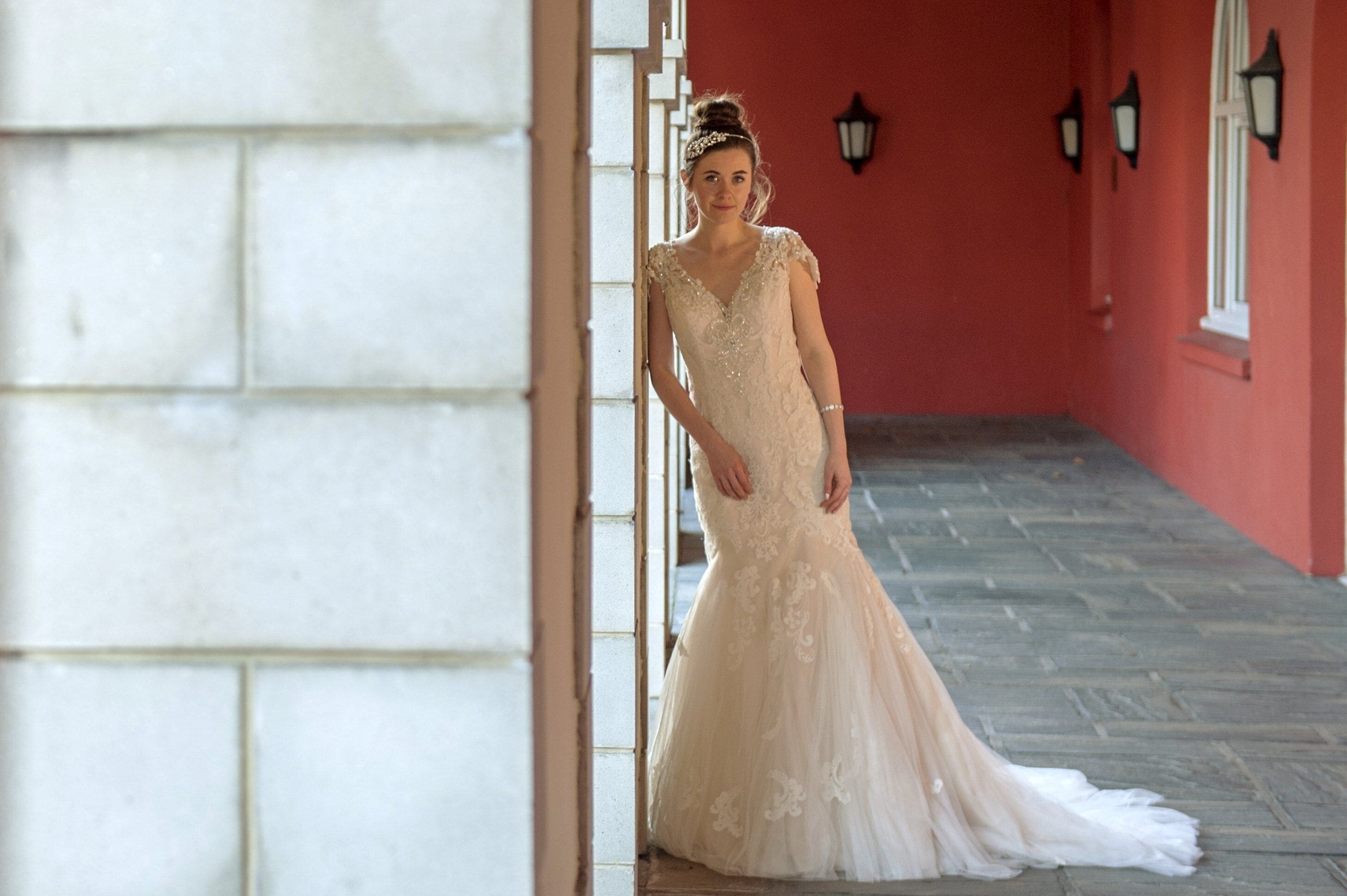A bride in a wedding dress standing in a hallway with a red wall and a white door.