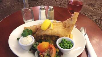 Un plato de pescado con patatas fritas y guisantes, una ensalada y una copa de vino tinto sobre una mesa.