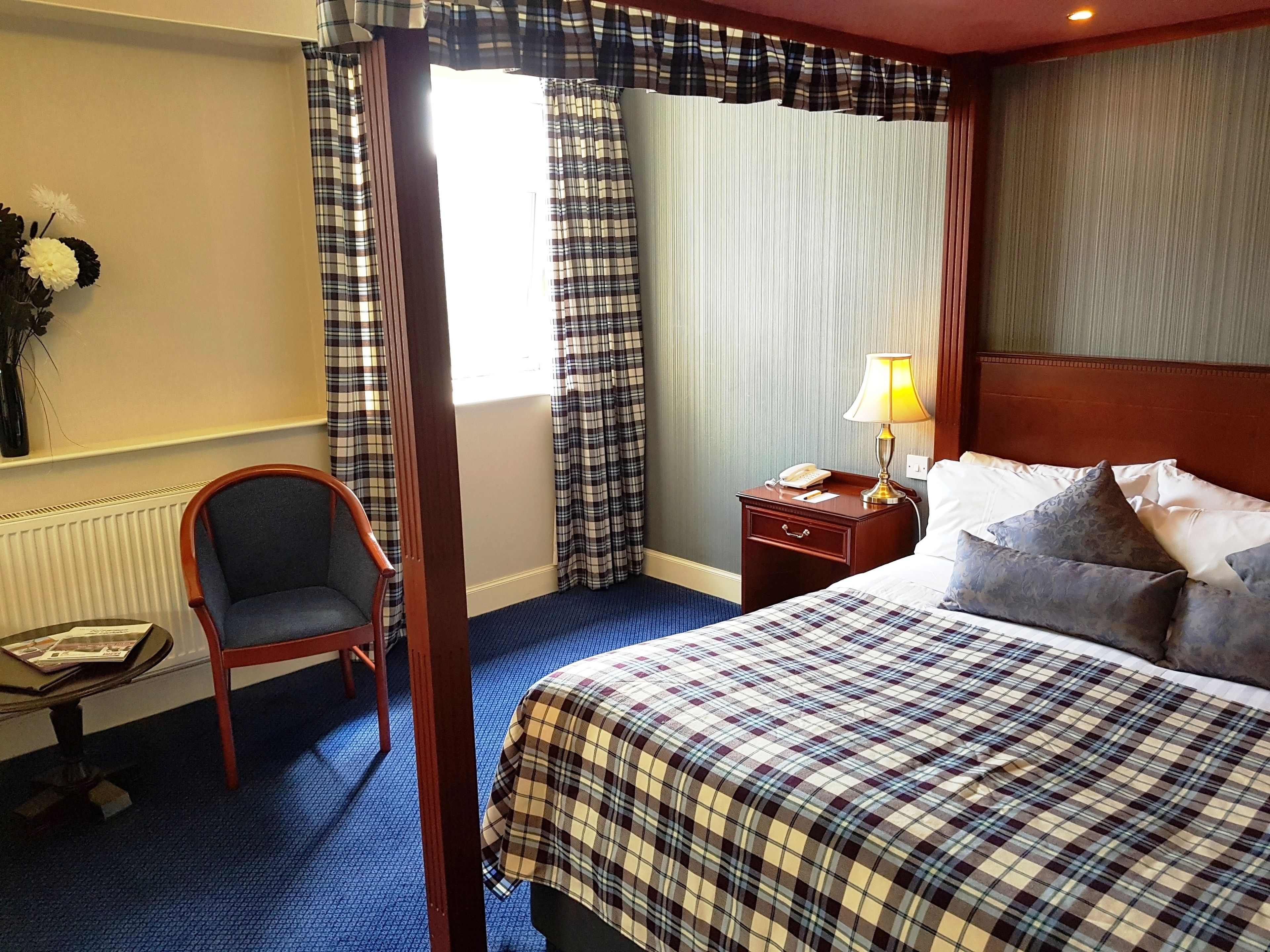 A hotel room with a bed, a chair, a nightstand with a lamp, and a window with curtains.