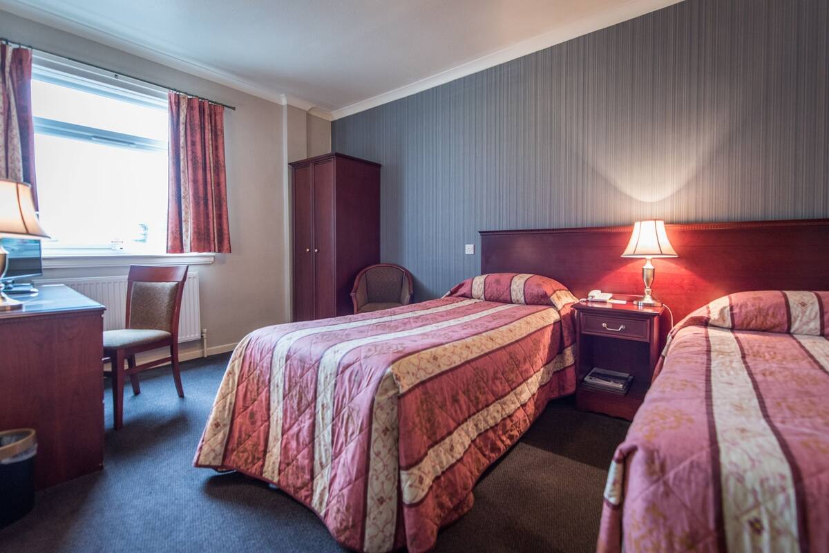 A hotel room with two beds, a desk, a chair, a wardrobe, and a lamp.