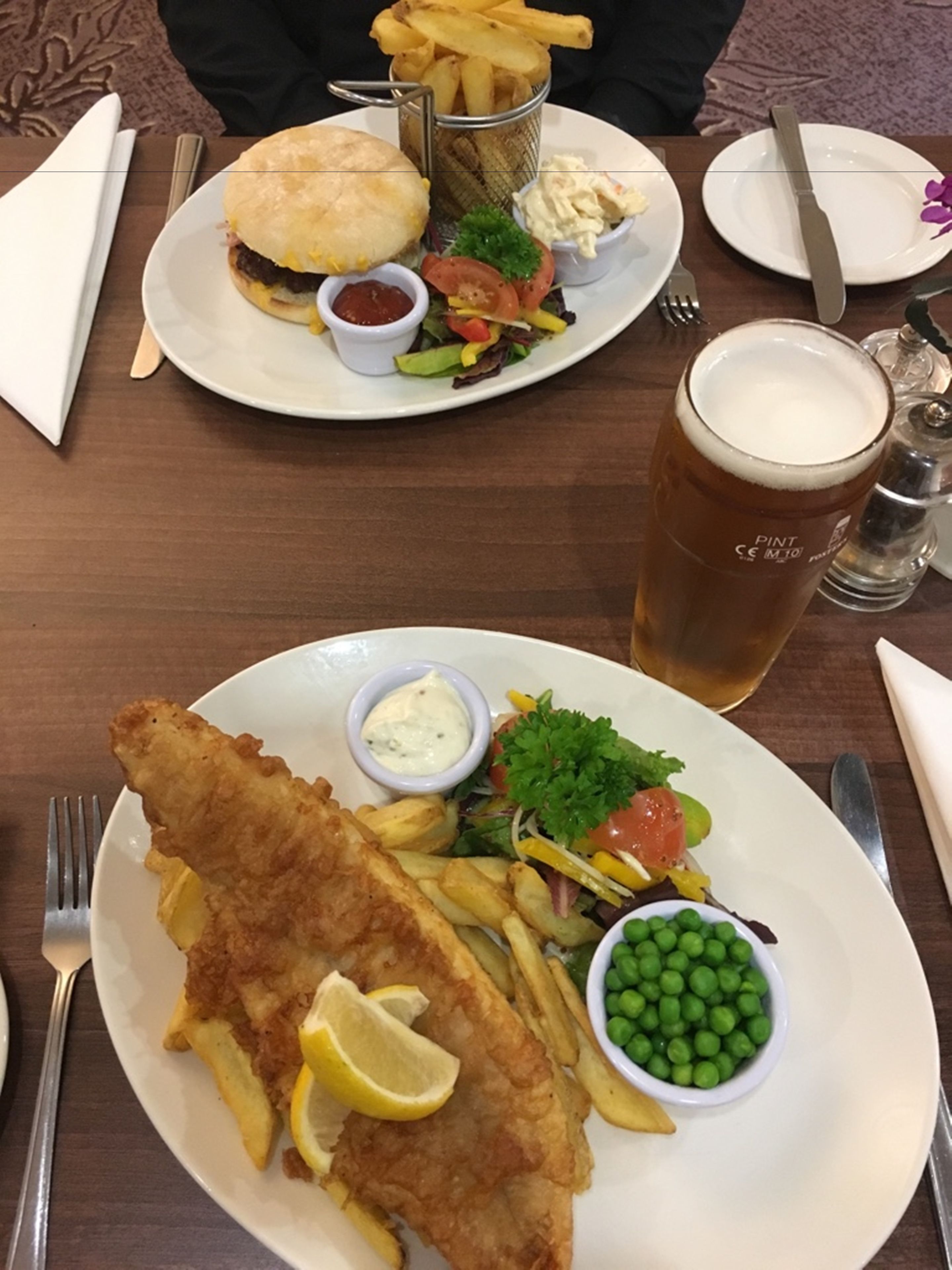 A meal consisting of fish and chips, a salad, and a glass of beer on a wooden table.