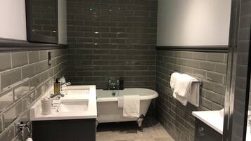 Un baño moderno con paredes de azulejos oscuros, un lavabo blanco, una bañera y un espejo sobre el lavabo.