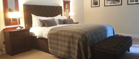 A neatly made bed with a plaid bedspread, two bedside lamps, a nightstand, and a bench.
