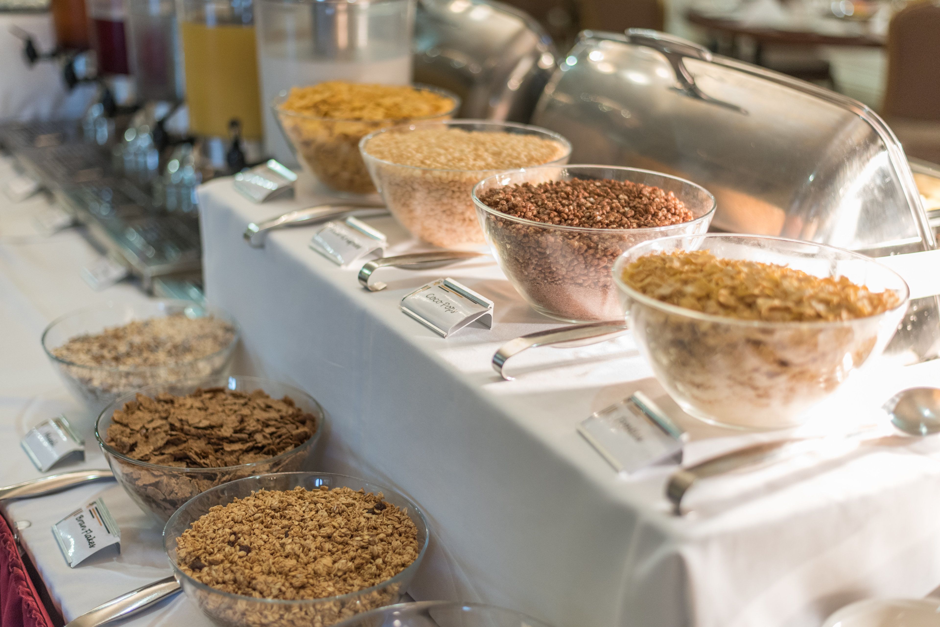 A buffet table with various food items in bowls, including cereals and granola.
