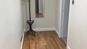 A hallway with wooden flooring, a coat rack, a mirror, and a door.