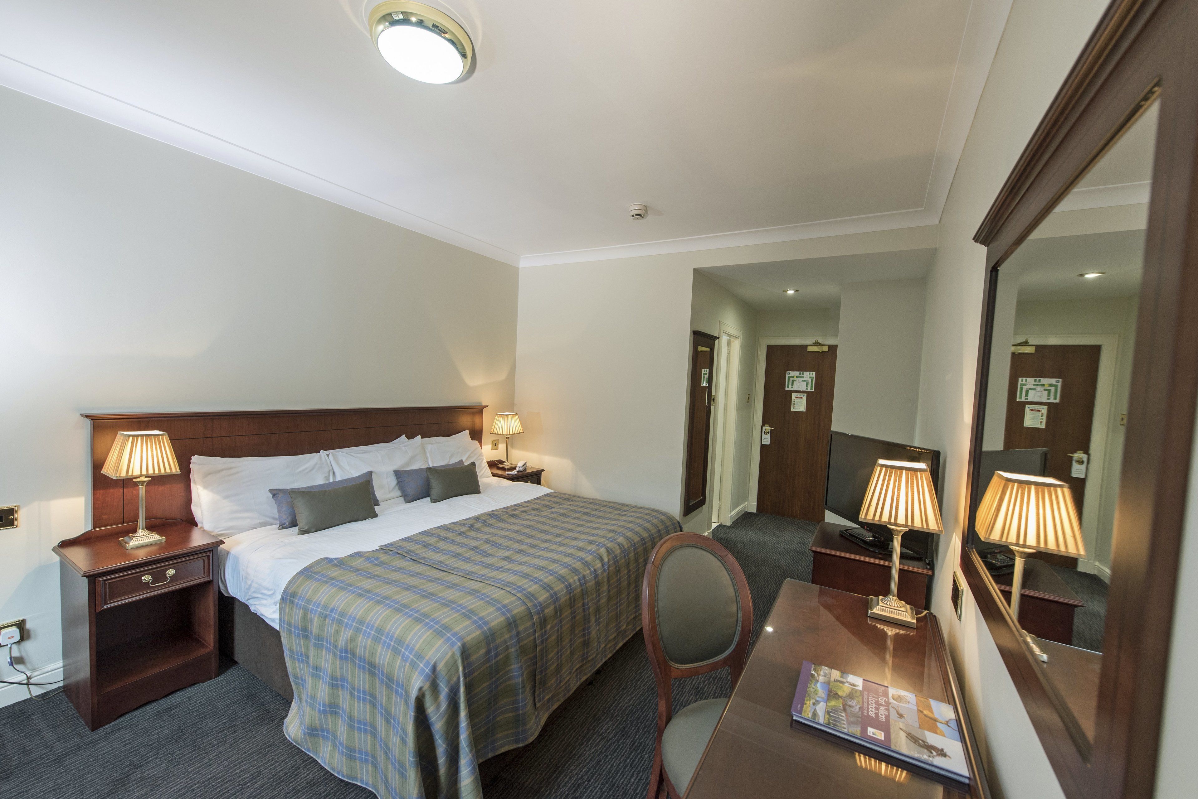 Une chambre d’hôtel comprenant un lit, des lampes de chevet, un bureau avec une lampe, une chaise et un miroir.