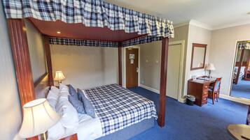 A four-poster bed with a plaid bedspread, a desk with a chair, a mirror, and a lamp.
