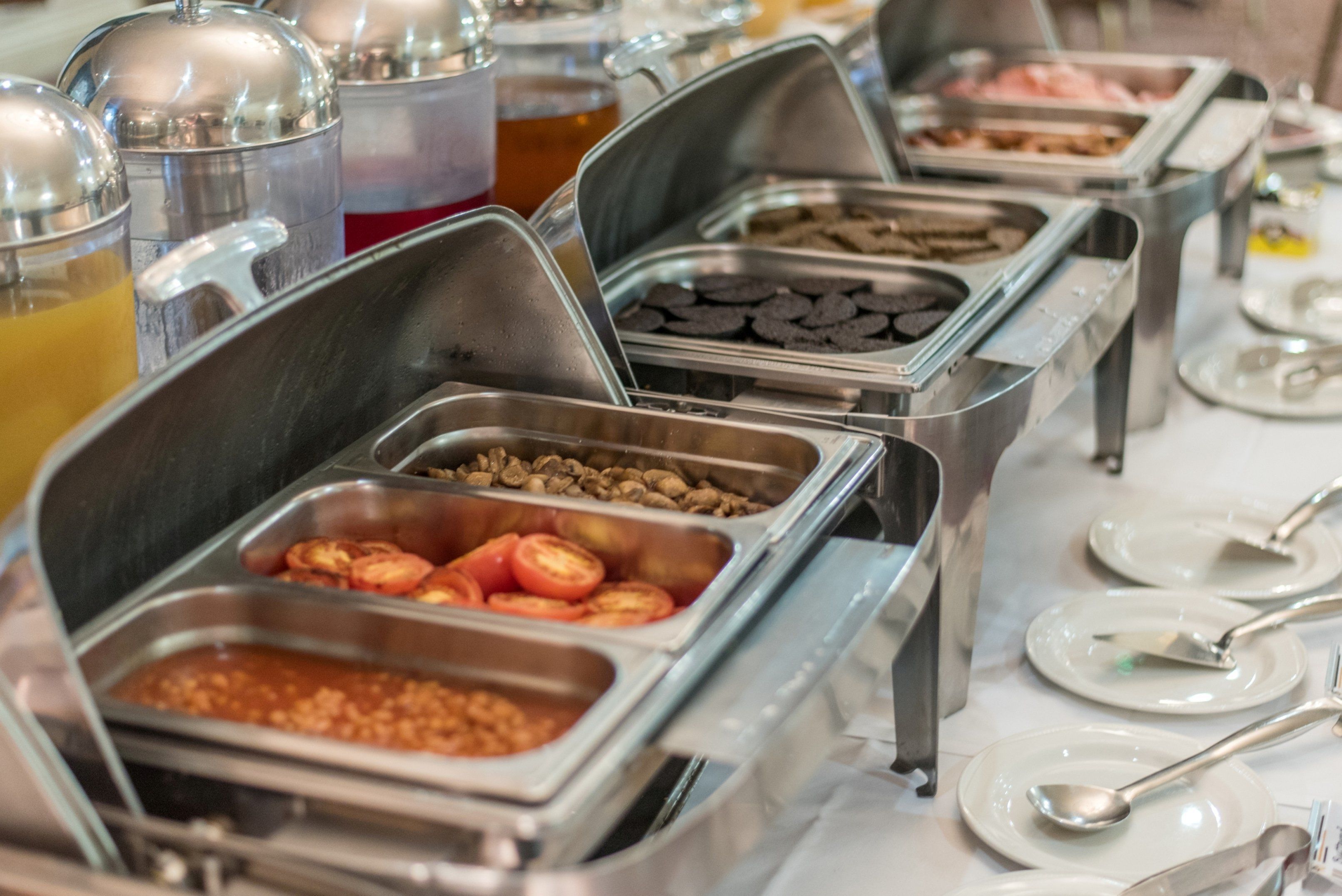 A buffet with various food items in metal containers, including fruits, vegetables, and different types of meats.