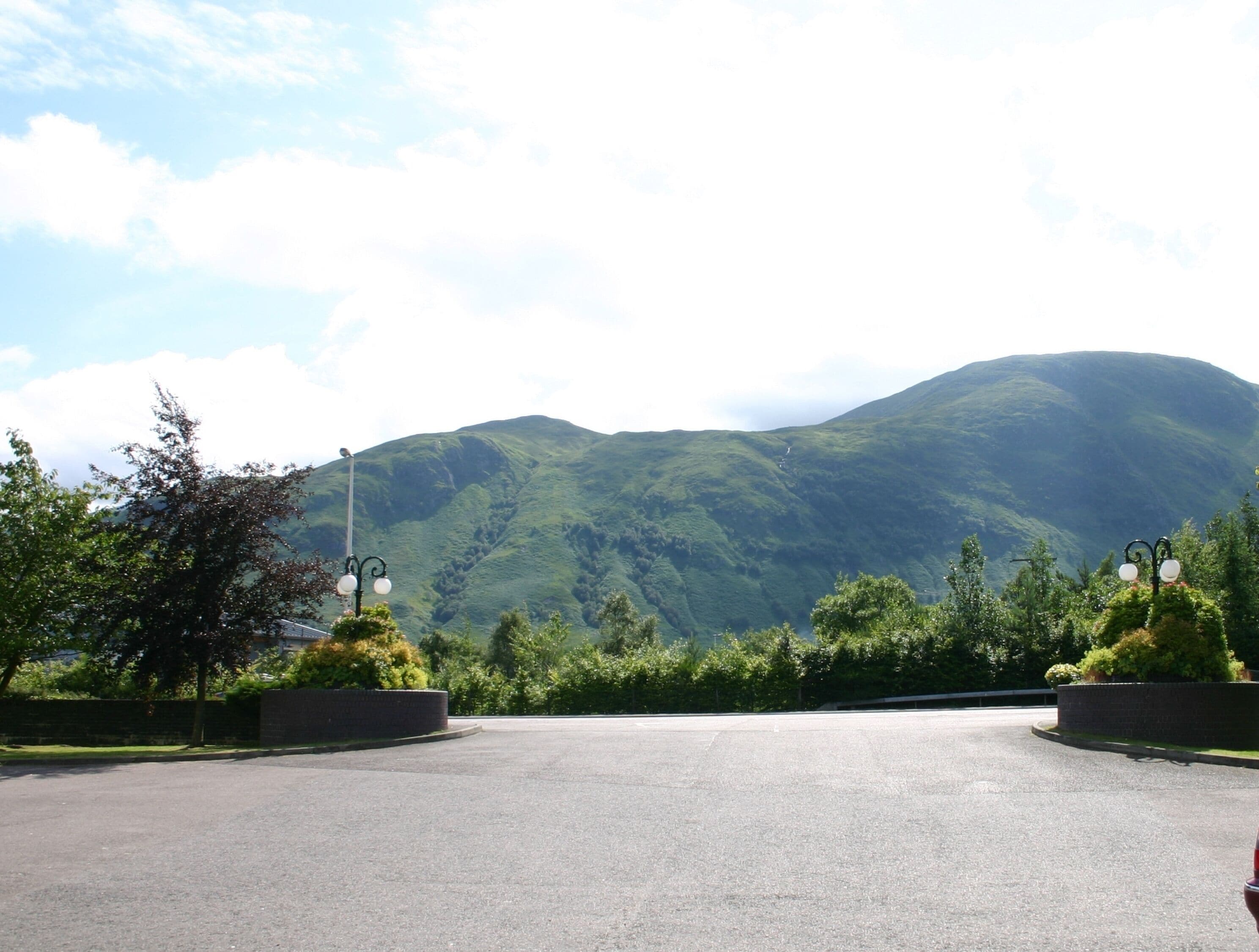 A parking area with a mountain backdrop, street lamps, and greenery.