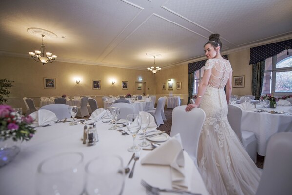 A banquet hall with round tables set for a formal event, chandeliers, and framed artwork on the walls.