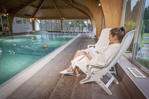 A pool area with a wooden ceiling, lounge chairs, and a person reading a book.