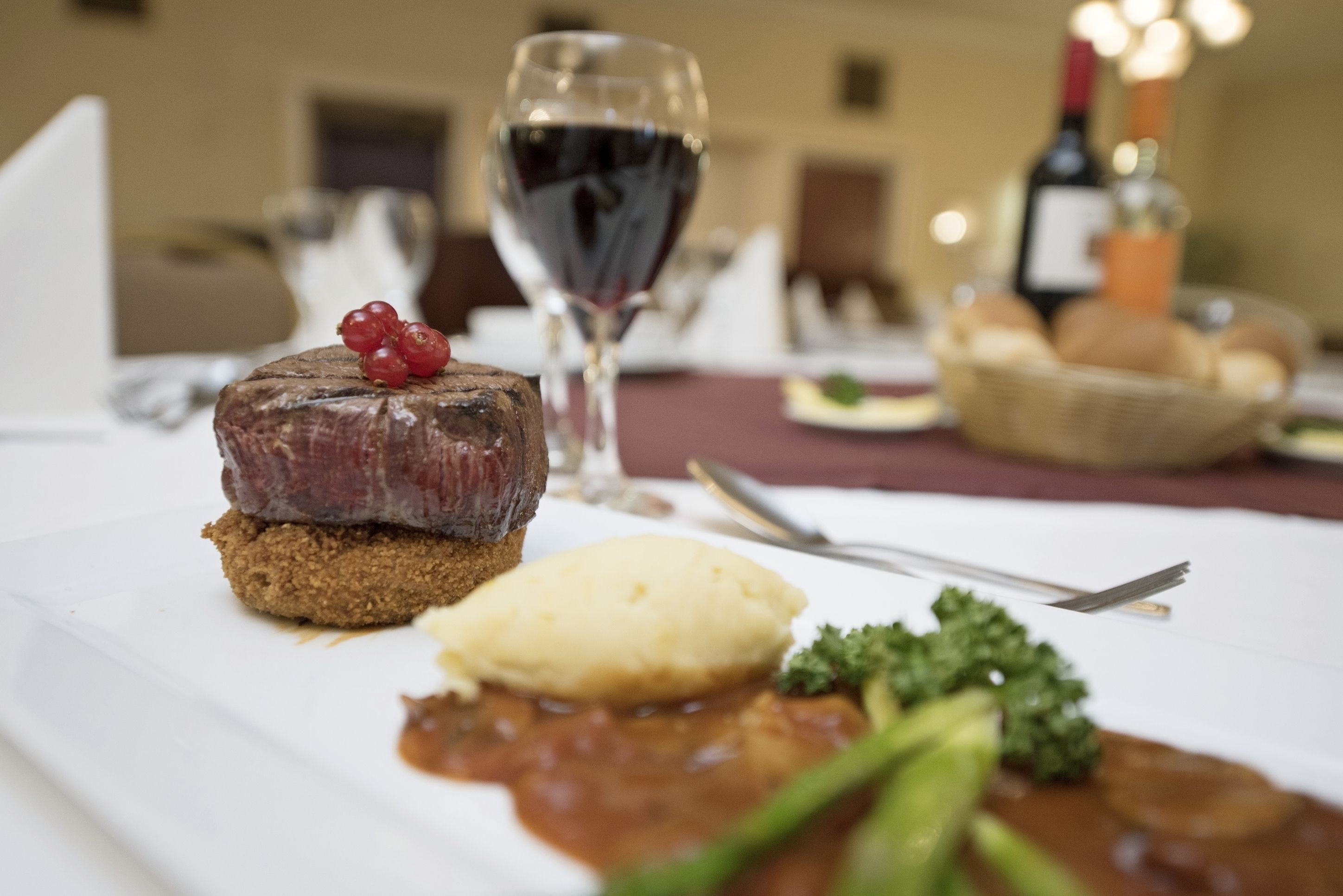 Un plato con filete, puré de papas y salsa, acompañado de una copa de vino tinto y una vela.