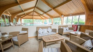 Un espace de détente extérieur abrité, avec des meubles en osier, une piscine et de grandes fenêtres.