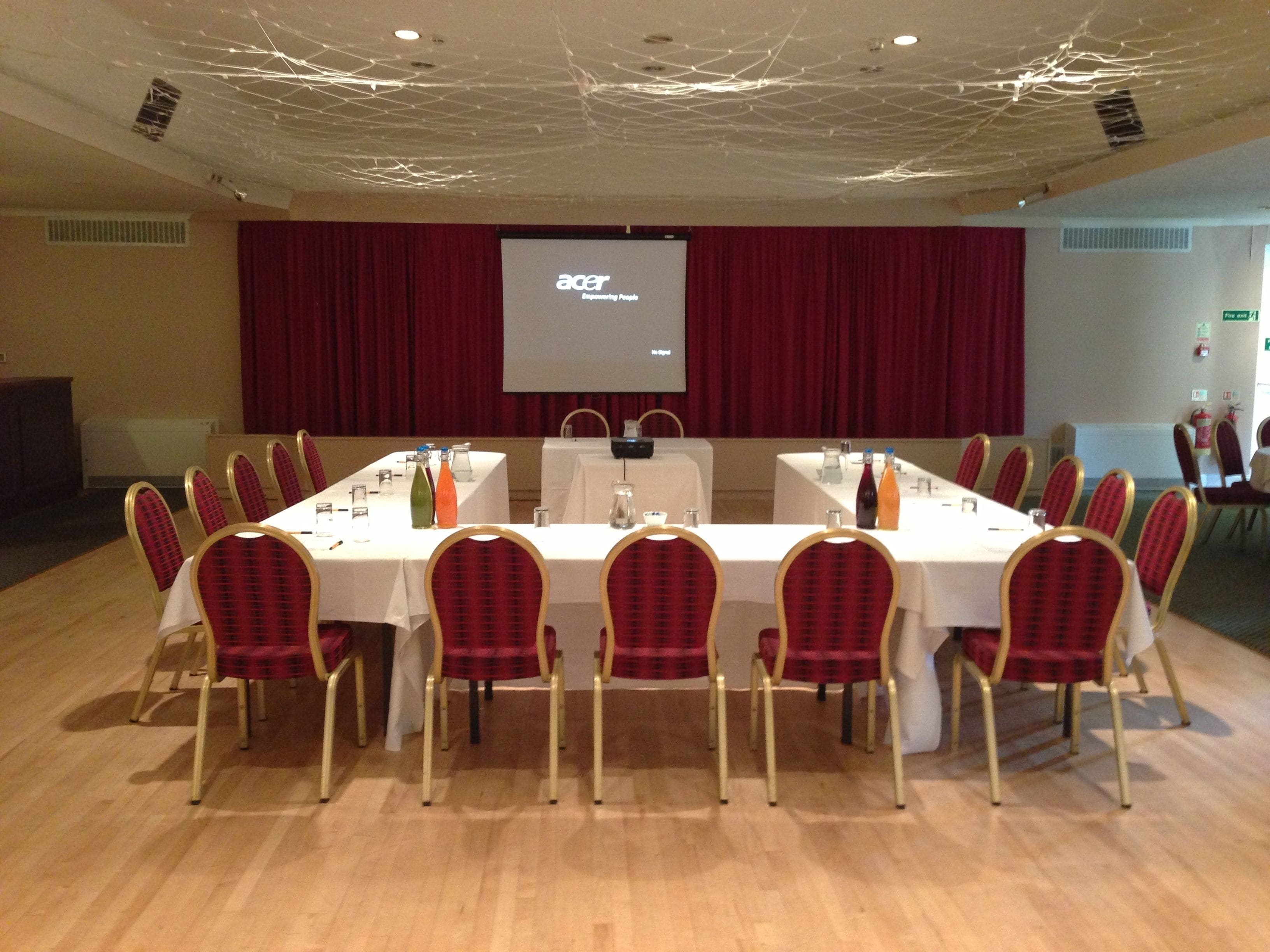 A conference room with a long table, red chairs, and a projector screen displaying 'Acer'.